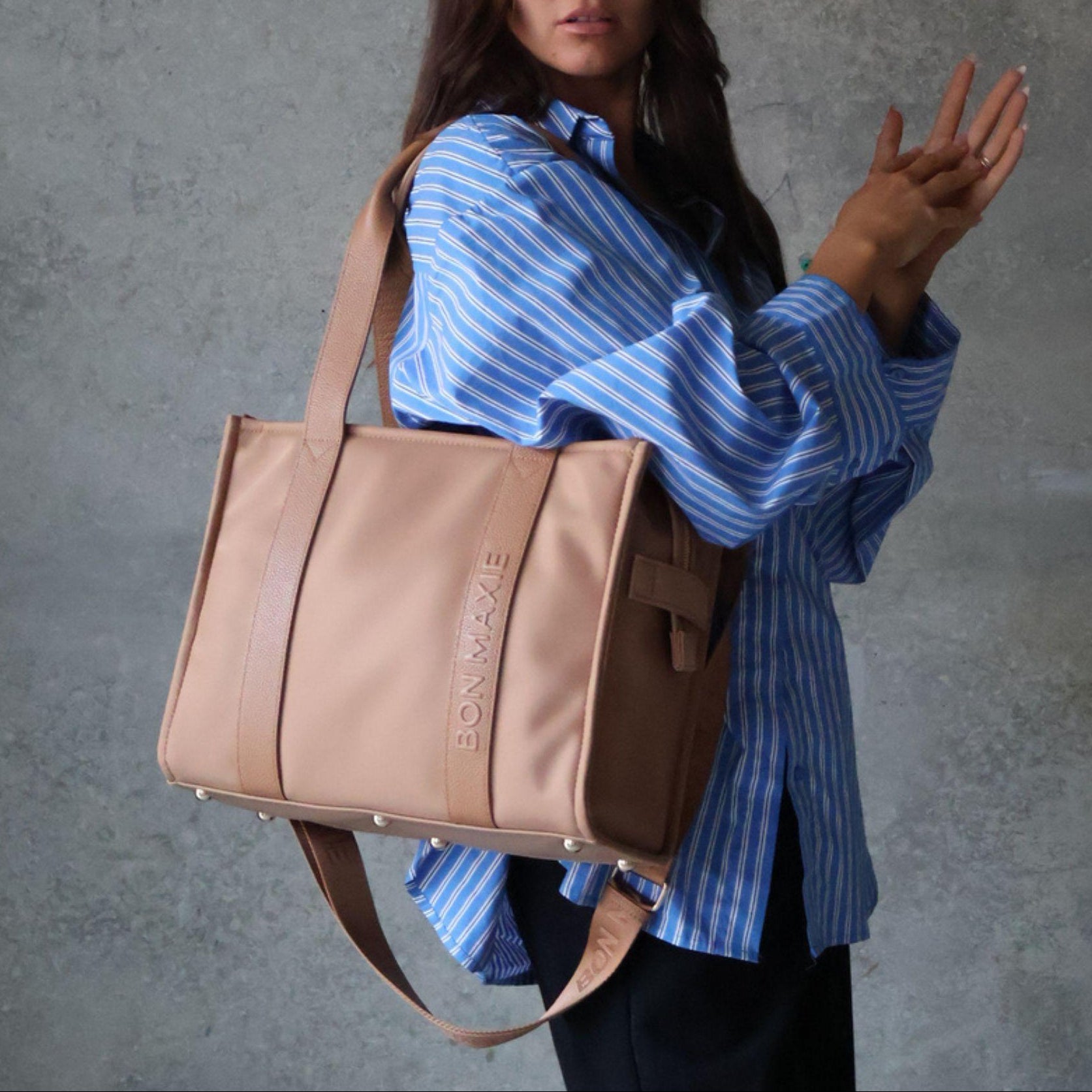 Woman holding a tan tote handbag with a brand logo against a gray background