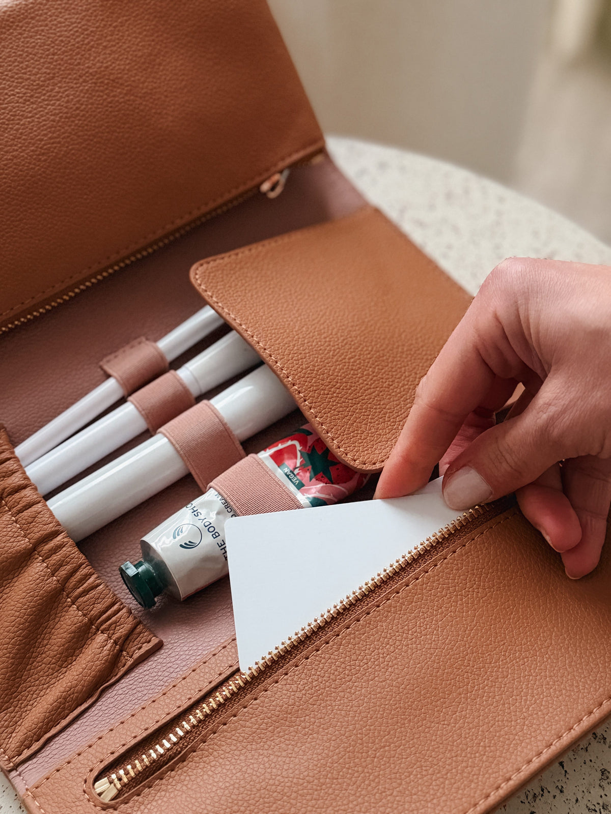 Hand pulling a card from the Marli Essentials Pouch Driftwood — interior slots filled with brushes and essentials