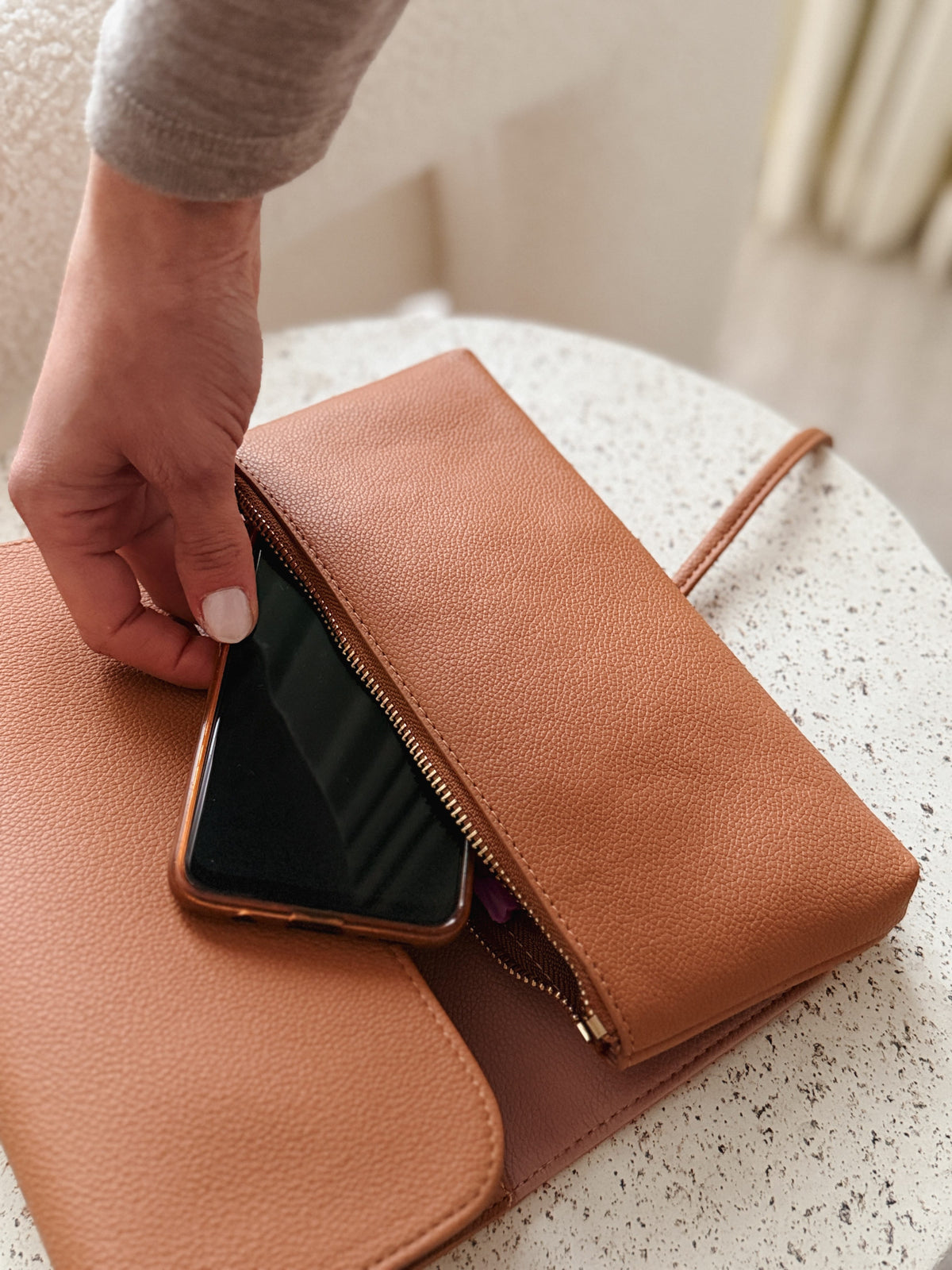 Hand sliding phone into the zip pocket of the Marli Essentials Pouch Driftwood