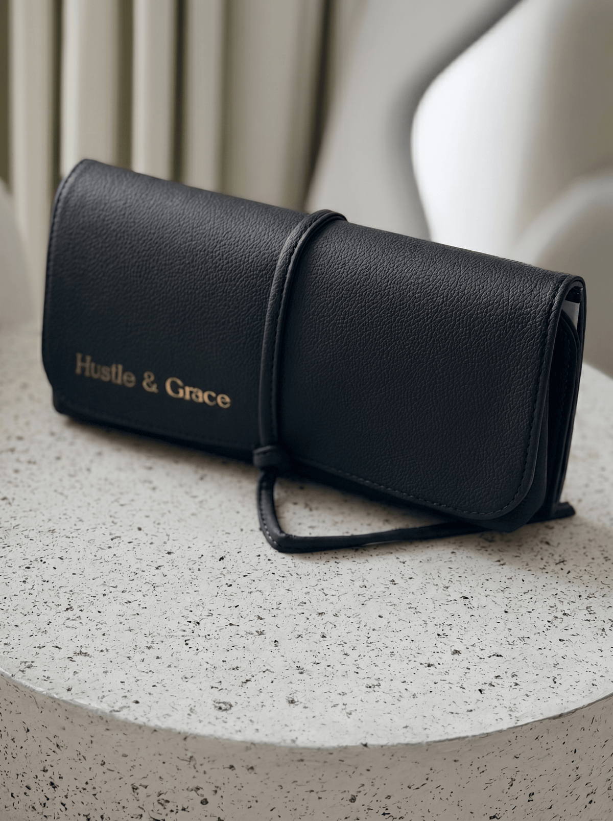 Marli Essentials Pouch in Charcoal with Hustle & Grace branding on a textured surface